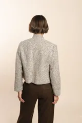 Chaqueta de sastrería color crudo con textura tweed, corte entallado, cuello mao y mangas largas.