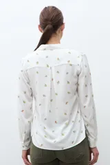 Camisa blanca de manga larga con cuello abotonado y estampado de pequeñas flores en tonos naranjas y verdes.