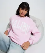 Buzo de algodón y poliéster color rosa claro, con cuello redondo y manga larga. Presenta un estampado grande en el frente con el texto "MALIBU CALIFORNIA BEACH" en letras blancas.