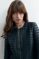 Chaqueta negra de eco cuero con detalles de tul en mangas y hombros, cierre frontal con cremallera dorada y corte ajustado.