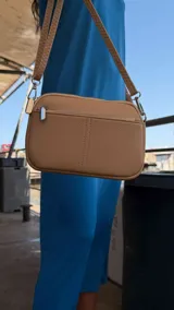 Bandolera pequeña de símil cuero color gris con textura granulada. Posee dos compartimientos principales con cierre y un bolsillo frontal con cremallera metálica. Incluye correa fina ajustable y extraíble.