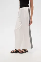 Pantalón blanco de viscosa, corte ancho y tiro alto, con detalle de bordado calado negro en los laterales.