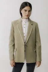 Blazer color camel de lana con solapas y cierre con botones. Presenta detalle de pespuntes blancos en los bordes.