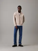 Buzo color beige de corte holgado, con cuello alto y cremallera corta. Tiene puños y bajo elásticos, y logo de Calvin Klein grabado en el pecho.