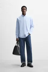 Camisa celeste de algodón, corte relaxed fit, cuello abotonado, manga larga con puños abotonados y cierre frontal con botones.