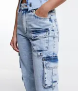 Pantalón recto de jeans celeste con cintura alta, bolsillos cargo laterales y detalle de aro metálico en la pierna.