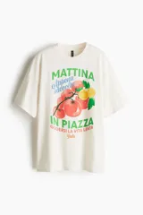 Remera oversized de algodón color crema con estampado de tomates y limones, y texto en italiano en verde y azul.