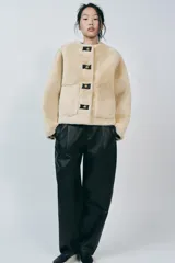 Chaqueta corta de cuello redondo y manga larga en tejido de pelo sintético color negro. Cierre frontal con botones metálicos dorados y bolsillos de plastrón. Colección Zara Woman.