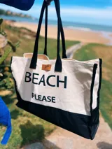 Bolso de playa grande de lona color crema con base negra y asas de soga negras. Estampado frontal con la frase "Beach Please" en letras negras.