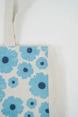 Bolso tote de tela con estampado de rayas verticales rosadas y blancas, laterales y asas en color beige. Presenta la palabra "BONJOUR" en verde en el centro y "INDIAN" en la parte inferior.