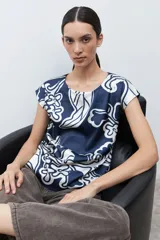 Blusa de manga corta con cuello redondo, confeccionada en tela satinada con estampado abstracto en azul marino y blanco.