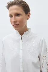 Camisa de algodón celeste claro, de manga larga, con cuello mao con volados y bordados calados florales en el frente y las mangas.