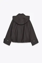 Trench corto color negro, con cuello solapa y capucha desmontable mediante botones. Manga larga tipo murciélago acabada en trabilla ajustable. Bolsillos laterales. Forro interior combinado. Cierre frontal con botones. Tejido repelente al agua.