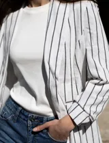 Blazer blanco con rayas verticales negras, cuello con solapa, bolsillos simulados y mangas 3/4 fruncidas. Forro interno blanco, marca Dictionary.