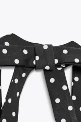 Vestido corto negro con lunares blancos, cuello halter y escote pico. Detalle de lazo en la espalda y cierre lateral con cremallera oculta.