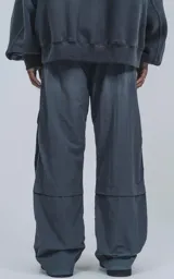 Pantalón cargo técnico gris oscuro, de silueta oversize y tejido liviano. Presenta múltiples bolsillos cargo con solapa en las piernas, uno de los cuales tiene una pequeña etiqueta negra con texto.