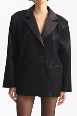 Blazer negro de silueta cuadrada, con cierre de un solo botón y solapas de satén. El cuerpo del blazer tiene un acabado brillante o de lentejuelas finas.