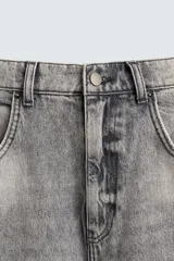 Pantalón de jean gris con lavado gastado, corte holgado, tiro medio, cinco bolsillos y roturas. Cierre frontal con cremallera y botón.