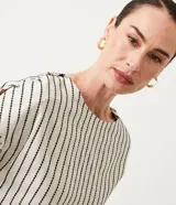 Blusa de algodón color blanco con rayas verticales negras, cuello redondo y botones decorativos en los hombros.