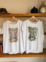 Remera blanca de algodón con cuello redondo y estampado de cerezas rojas con hojas verdes y texto dorado.