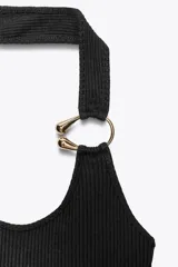 Top negro de tejido rib con escote asimétrico, manga sisa y tirante ancho con detalle de aro metálico dorado.