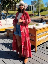 Vestido camisero largo con estampado floral en tonos rojos y blancos, con botones frontales, mangas largas abullonadas y cinturón con hebilla dorada.