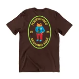 Remera marrón de manga corta con estampa en la espalda de un sapo vestido con campera y pantalón, dentro de un óvalo con el texto "Puerto Rico Seguimos Aquí 20 25".