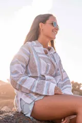 Buzo con capucha a rayas horizontales en tonos beige, blanco y celeste. Tiene un bolsillo tipo canguro en la parte delantera y cordones ajustables en el cuello.
