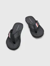 Ojotas negras Tommy Hilfiger con tira ancha de poliuretano acolchada y suela de goma EVA. Detalle de cinta distintiva con los colores de la marca en la tira.