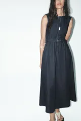 Vestido midi de denim azul oscuro, sin mangas, con cuello redondo, bolsillos laterales, cinturón con hebilla metálica y cierre frontal con cremallera.