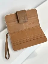 Billetera grande de cuero rosa con cierre de cremallera y correa de muñeca marrón. Tiene un aplique marrón con el logo de la marca en el frente.