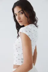 Top de manga corta en punto pointelle blanco con estampado floral diminuto en tonos rosados. Presenta cuello redondo con tapeta de botones.