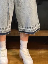 Bermuda de jean celeste matizado, corte baggy, con cordón ajustable en la cintura y detalle artesanal visible en el bajo.