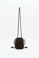 Bolso tipo saco o 'bucket bag' de terciopelo con estampado animal print en tonos marrón oscuro y negro. Presenta costuras verticales en hilo dorado y cordones ajustables negros con borlas y cuentas doradas en los extremos.