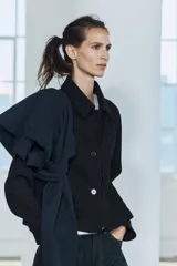Chaqueta corta negra de cuello solapa y manga larga con puños. Tiene bolsillos de parche en el frente y cierre frontal con botones.