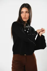 Buzo negro con cuello y manga campana, adornado con tachas en el dobladillo, confeccionado en tejido sintético suave.