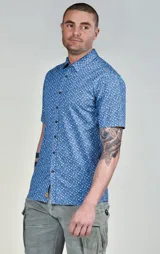 Camisa de manga corta celeste con estampado de flores blancas, cuello clásico y cierre frontal con botones. Corte recto.