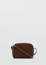 Bolso pequeño de piel bovino color marrón oscuro, con acabado en serraje (gamuza). Presenta un forro interior de algodón y cierre principal de cremallera. Incluye un asa larga ajustable.