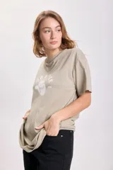 Remera color arena de corte oversize con estampa de un sombrero de cowboy y la frase "Wild & Free" en blanco.