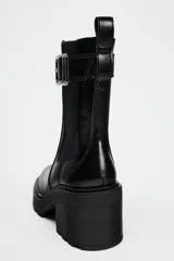 Botín negro estilo Chelsea con elástico lateral, hebilla decorativa y suela track con tacón bloque.