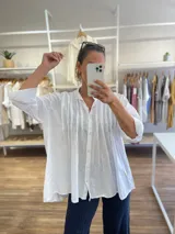 Camisa blanca de algodón, con cuello abotonado y detalles de pinzas verticales en el frente. Manga 3/4 con puño amplio.