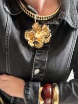 Collar con cordón trenzado de cuero sintético color negro, con dije circular plateado con centro de piedra blanca con pintitas negras. Cierre con mosquetón plateado.