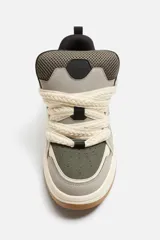 Zapatilla deportiva estilo skate color gris y verde, con cordones anchos color crema, lengüeta acolchada, tirador trasero y suela gruesa de goma color caramelo.