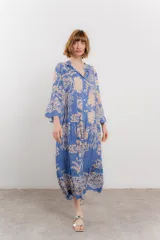 Vestido largo azul con estampado floral en tonos beige, confeccionado en viscosa. Presenta escote en V, botonadura completa en el frente y mangas largas con volados.