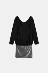 Vestido corto con parte superior negra de manga larga y escote barco drapeado, y falda corta de lentejuelas plateadas.