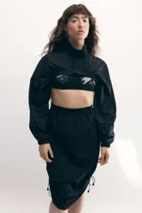 Campera cropped negra de tela técnica, con cuello alto, mangas murciélago y cierre frontal al tono.