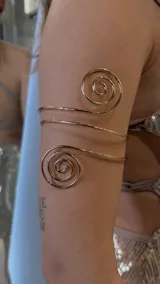 Brazalete dorado de metal con diseño de espirales.