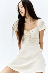 Vestido corto color crema, de punto acanalado, con escote corazón ribeteado en encaje y cordón para ajustar en el centro del busto. Modelo de manga corta con cuerpo entallado y falda con vuelo.