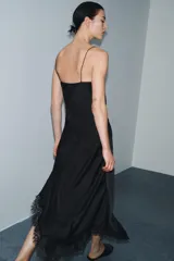 Vestido lencero de satén negro, corte midi asimétrico, con escote fluido y tirantes finos. Presenta drapeado lateral y aplicación de encaje a tono en el bajo.