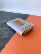 Billetera pequeña con cierre metálico, cuerpo principal de cuero lila texturizado y ribetes en color crema. Presenta un parche de cuero marrón con la palabra "chowie" escrita en cursiva.